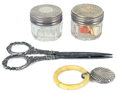 Lot 110 - A pair of Victorian silver lidded glass jars, a pair of silver-handled scissors and a baby's rattle.