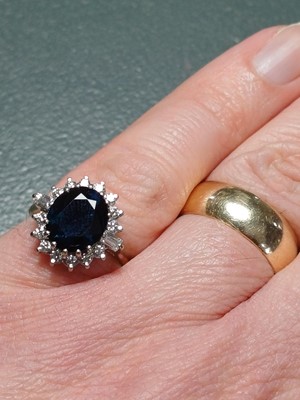 Lot 132 - An 18ct oval blue sapphire and diamond cluster ring.
