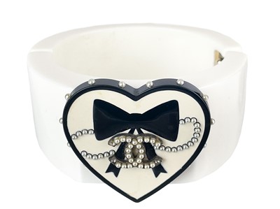 Lot 530 - A Chanel CC heart and bow applied, white and black resin cuff hinged bangle, circa 2006.