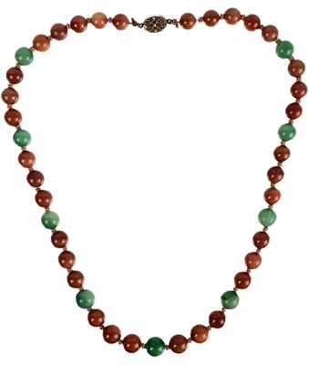 Lot 1085 - A Chinese green and russet jade bead necklace with silver filigree clasp.