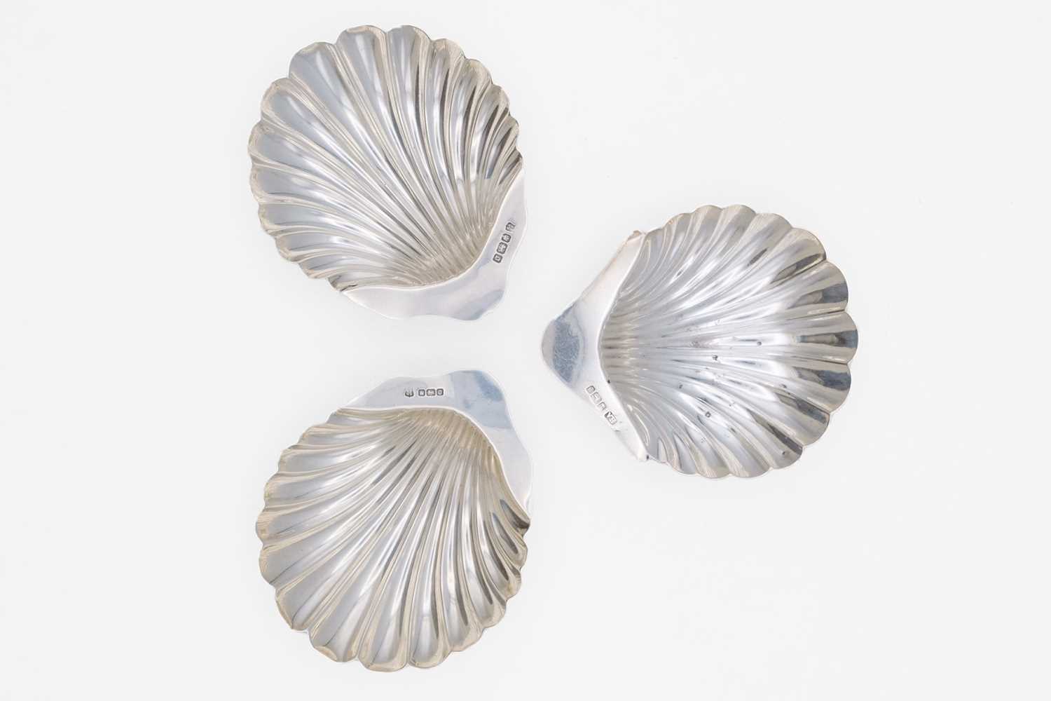 Lot 35 - An Edwardian silver pair of scallop shell butter dishes by James Deakin & Sons, and one other.