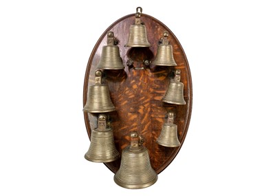 Lot 1319 - An early 20th century set of eight bells mounted on an oval oak wall plaque.