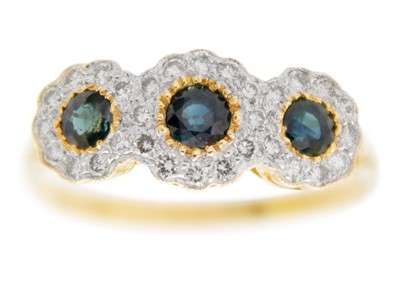 Lot 244 - An 18ct three-stone blue sapphire and diamond cluster trilogy ring.