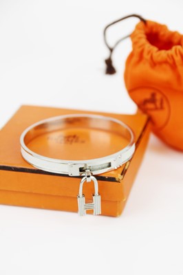 Lot 331 - HERMES - A Kelly H lock charm bangle in white metal and white leather.