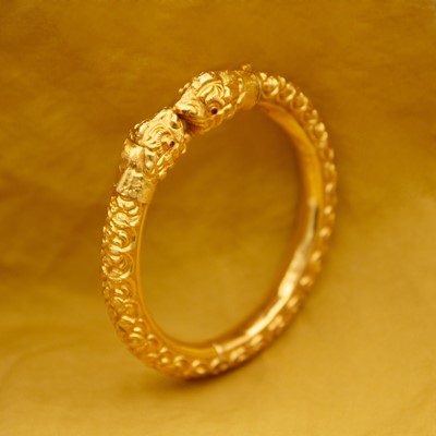 Lot 32 - A traditional Indian 22k gold hinged banhel kada bangle with lion head terminals and ruby eyes.