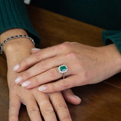 Lot 197 - An 18k white gold, emerald, and diamond cluster ring.
