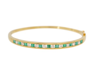 Lot 136 - An 18k gold emerald and diamond hinged bangle.