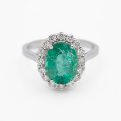 Lot 86 - An attractive 18k white gold emerald and diamond cluster ring.