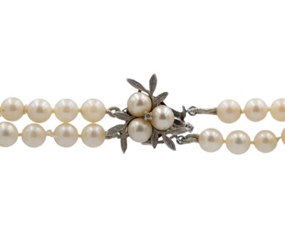 Lot 153 - A double-row cultured pearl necklace, strung to a 14k white gold diamond and pearl set clasp.