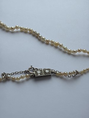 Lot 115 - A graduated pearl necklace strung to a white gold clasp set with two old mine-cut diamonds.