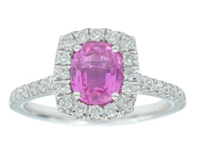 Lot 141 - A platinum ring set with an oval pink sapphire surrounded by melee diamonds.