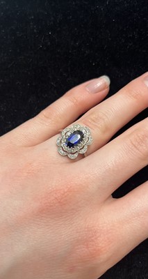 Lot 8 - An Art Deco oval blue sapphire and millgrain diamond set white metal cluster ring.