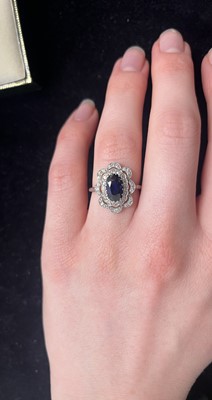 Lot 8 - An Art Deco oval blue sapphire and millgrain diamond set white metal cluster ring.
