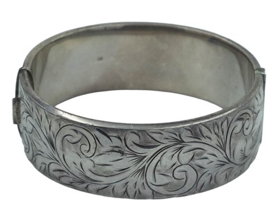 Lot 501 - A heavy silver hinged bangle with foliate scroll engraved decoration.