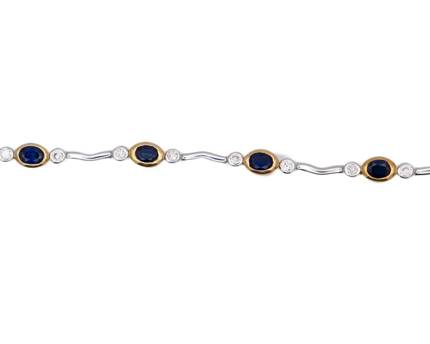 Lot 45 - A modern 18k yellow and white gold oval blue sapphire and diamond set bracelet.