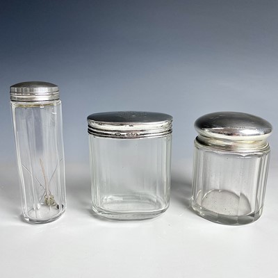 Lot 95 - Three glass toilet jars with silver lids,...