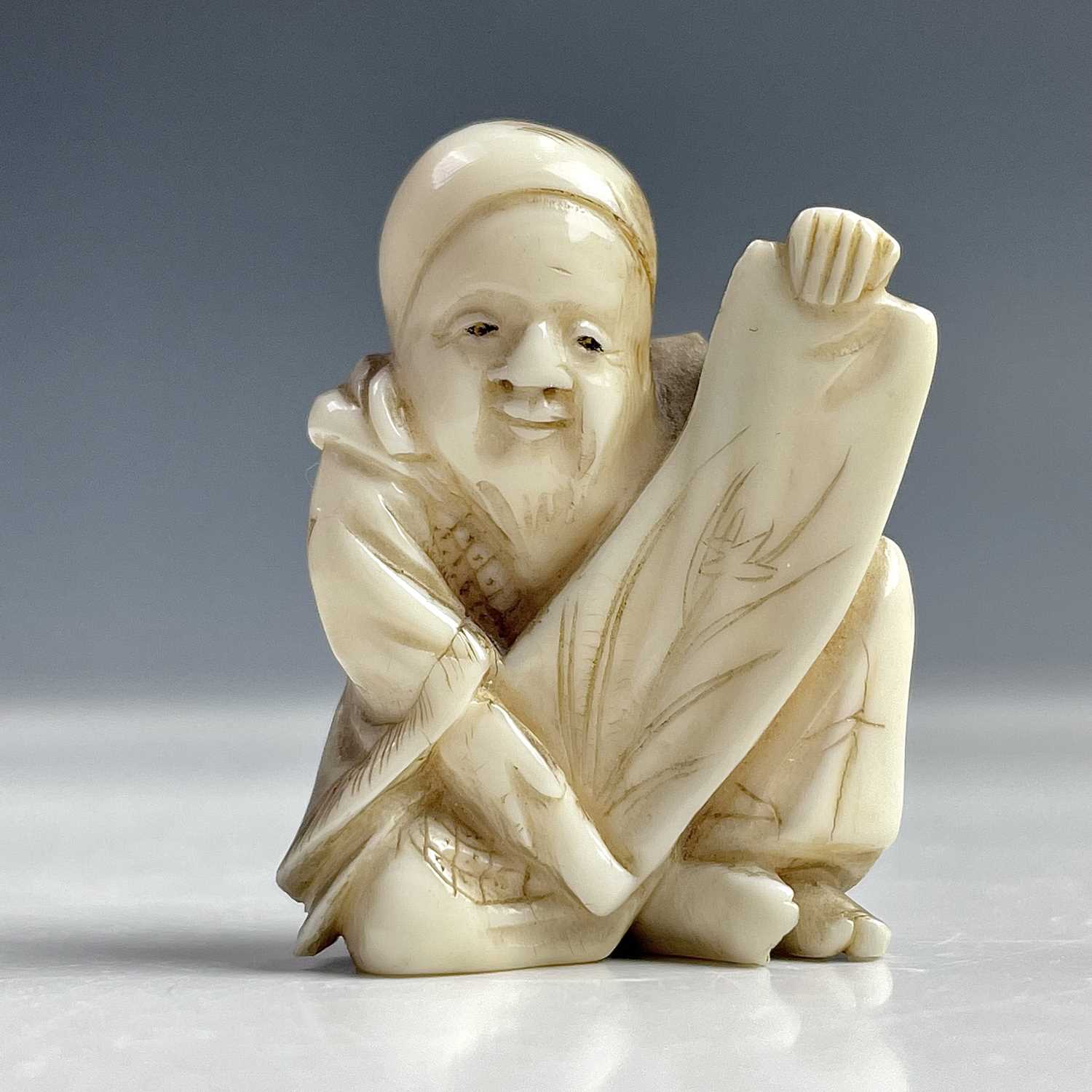 Lot 547 - A Japanese netsuke of a seated man holding a...