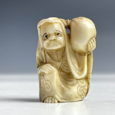 Lot 553 - A Japanese ivory netsuke of a man holding a...