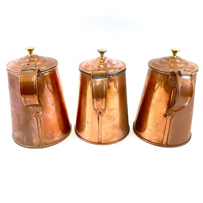 Lot 92 - A set of three copper jugs and covers with brass finials.