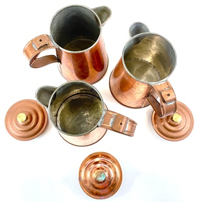 Lot 92 - A set of three copper jugs and covers with brass finials.
