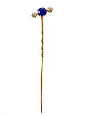 Lot 352 - A gold stick pin set with a sapphire and two diamonds.