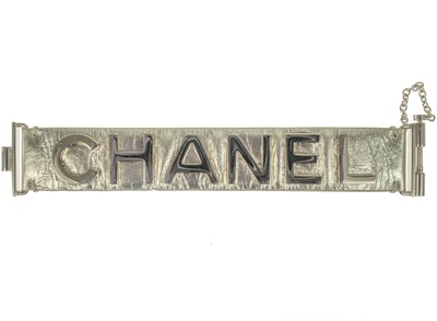 Lot 583 - A Chanel light gold tone and gold calfskin leather logo bracelet.